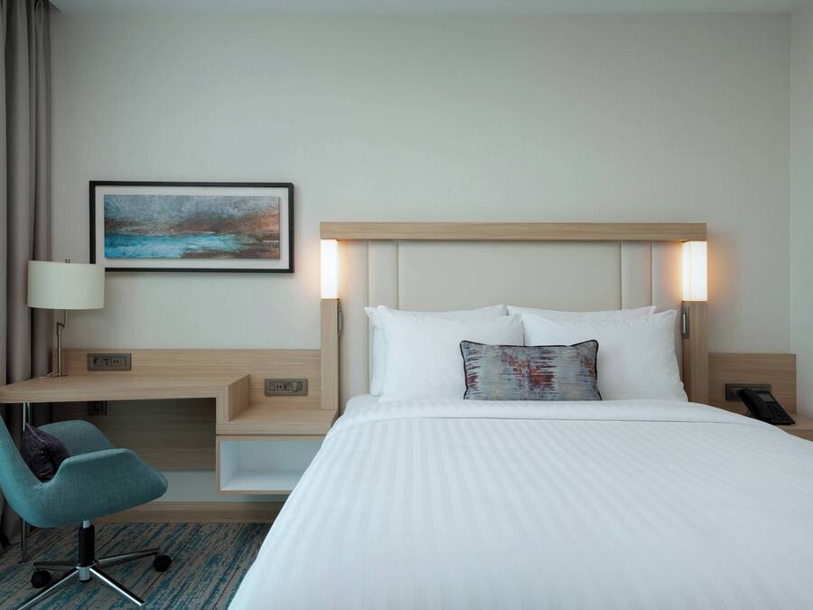 Habitación de hotel con cama, escritorio, silla, un cuadro y mesita de noche con teléfono.