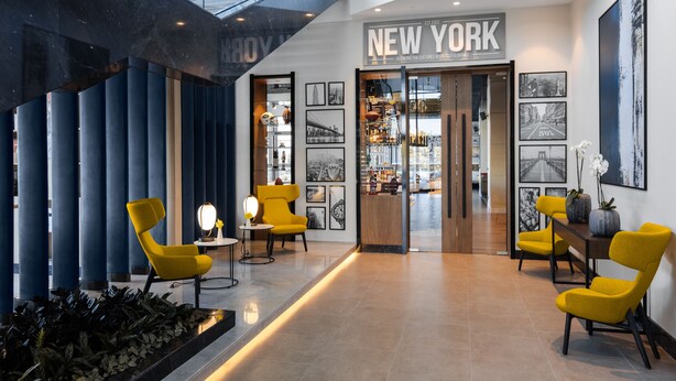 Un vestíbulo moderno con un cartel que dice 'NEW YORK', zona de estar y una escalera.