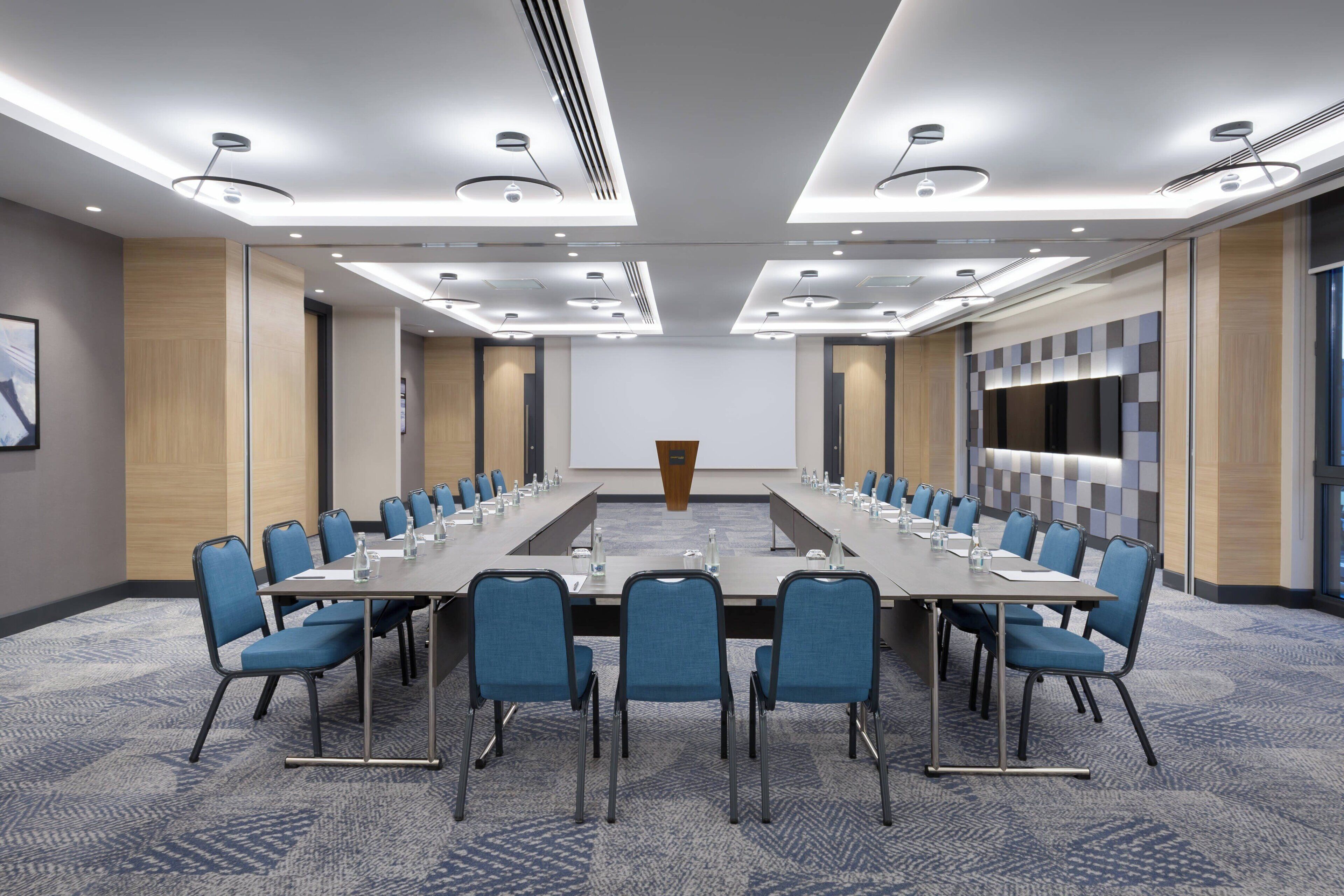 A conference room with a long table, blue chairs, and modern lighting.