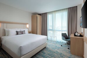 Une chambre d’hôtel avec un grand lit, un bureau avec une chaise, une télévision et une fenêtre avec des rideaux.