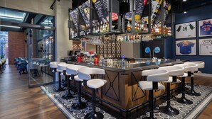 Una zona de bar con una barra larga, varios taburetes y una amplia variedad de botellas y vasos.