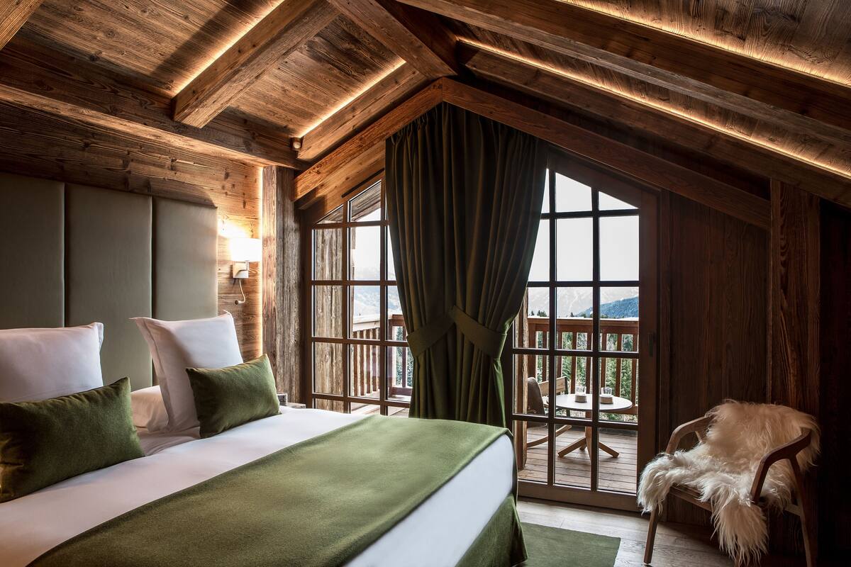 Een slaapkamer met een groot bed, uitzicht op het landschap en houten balken in het plafond.