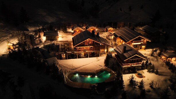 Un chalet enneigé comprenant plusieurs cabanes en bois, un bâtiment principal doté d’un balcon et une piscine.