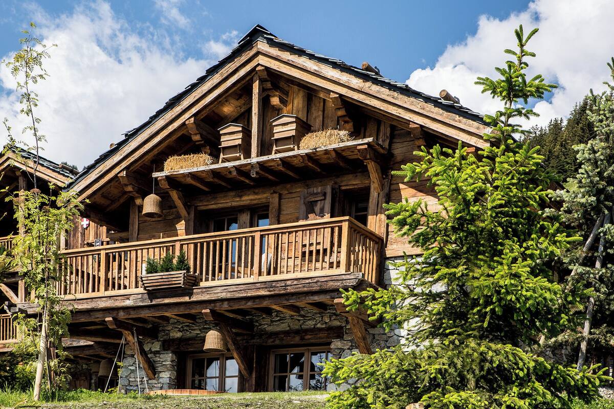 Een houten chalet met balkon, stenen fundering en omliggend groen.