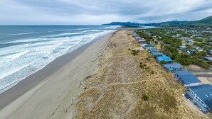 A coastal area with a sandy beach, a row of houses with blue roofs, and a hilly landscape in the background.