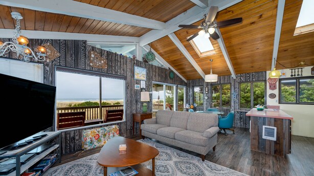 A spacious living room with a large TV, wooden ceiling, and a view of the outdoors.