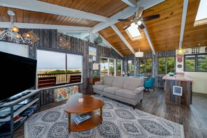 Amplia sala de estar con televisor grande, techo de madera y vistas al exterior.