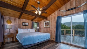 A wooden-paneled bedroom with a bed, ceiling fan, and large window with curtains.