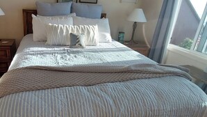 A neatly made bed with a quilted blanket, two bedside tables with lamps, a wooden dresser, and a window with curtains.