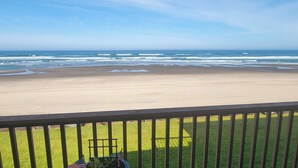 A beach view from a balcony with a railing, a grassy area, and a clear sky.