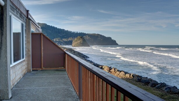 A balcony with a view of the ocean and a forested hill.