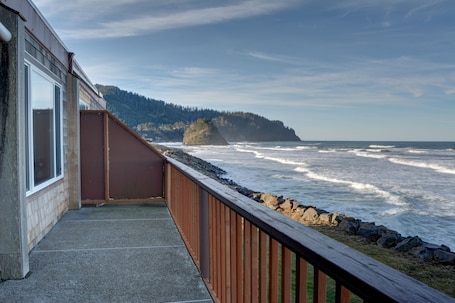 A balcony with a view of the ocean and a forested hill.