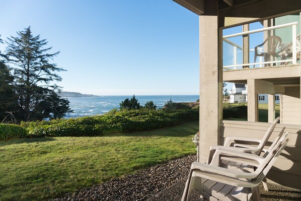 A balcony with outdoor furniture overlooking a grassy area and a view of the ocean.