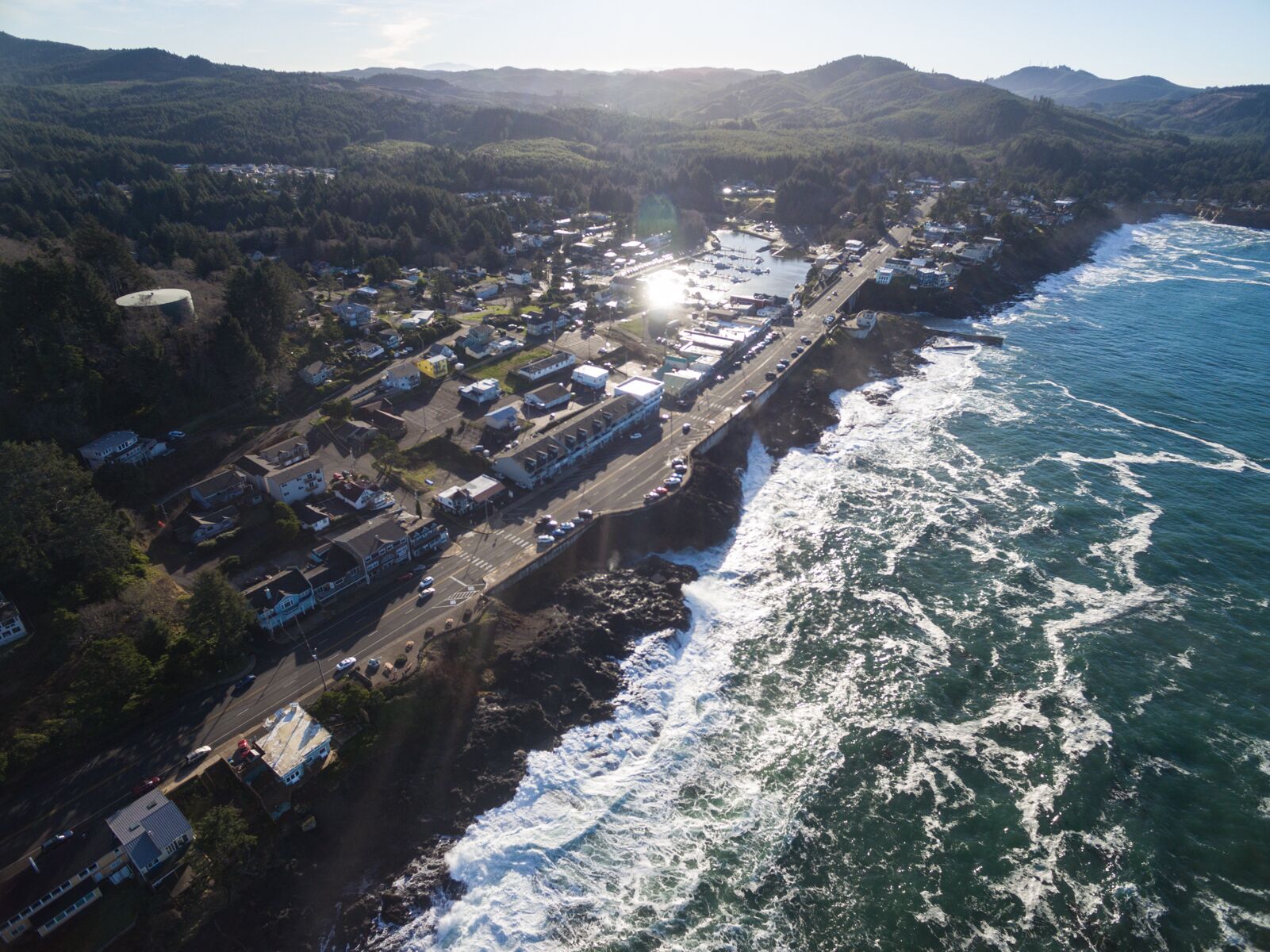 An aerial view of a coastal town with a road running parallel to the shoreline, a marina, and residential buildings.