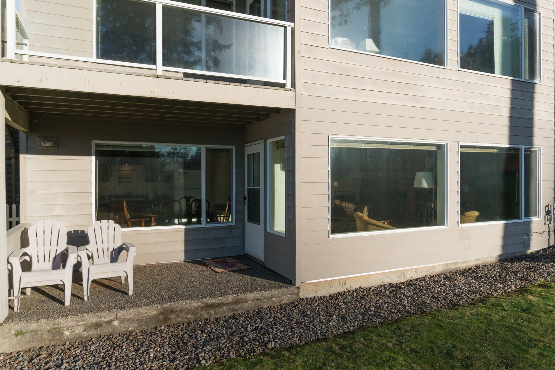 Ein modernes, zweistöckiges Haus mit überdachter Veranda, großen Fenstern und einem Kiesweg.