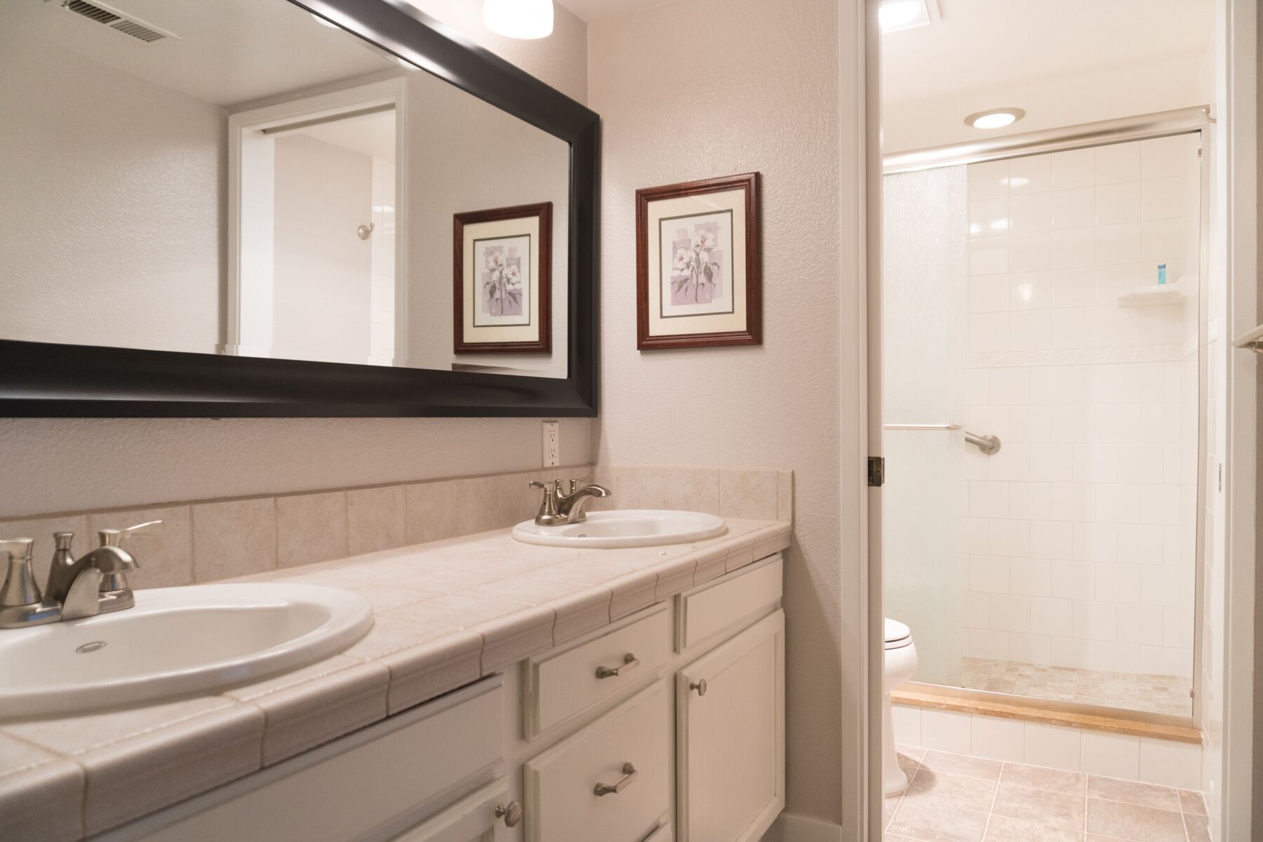 A bathroom with two sinks, a large mirror, and a shower area.