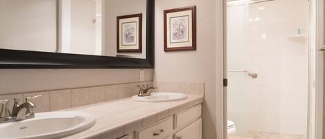 A bathroom with two sinks, a large mirror, and a shower area.