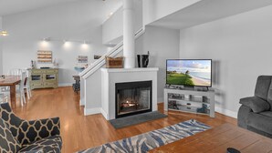 Una sala de estar moderna con chimenea, televisor y una escalera que sube a un nivel superior.