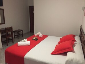 A hotel room with a bed, red pillows, a red bedspread, a small table, a chair, and a mirror on the wall. - Hotel Florida (Sanxenxo)