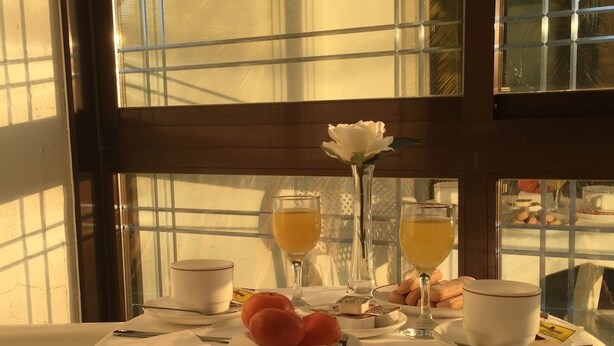 A breakfast table set with two glasses of orange juice, a white rose, pastries, and a small vase. - Hotel Florida (Sanxenxo)