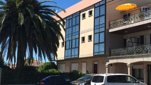A multi-story building with large windows, a balcony with a yellow umbrella, and parked cars. - Hotel Florida (Sanxenxo)