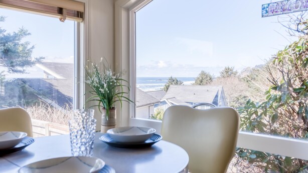 Un área de comedor con una mesa lista para dos personas, con vistas a un paisaje de casas y árboles.