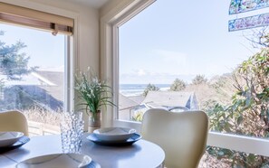 Un área de comedor con una mesa lista para dos personas, con vistas a un paisaje de casas y árboles.