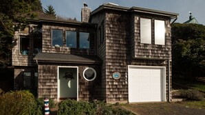 Une maison en bois à deux étages, dotée d’un garage, d’une fenêtre ronde et d’un petit porche.