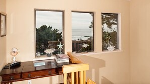Une pièce comprenant un bureau, une chaise et trois fenêtres donnant sur une plage.