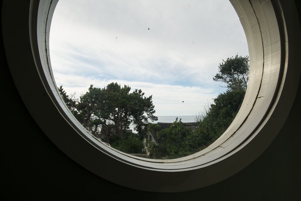 Une fenêtre ronde offrant une vue sur les arbres et un ciel nuageux.