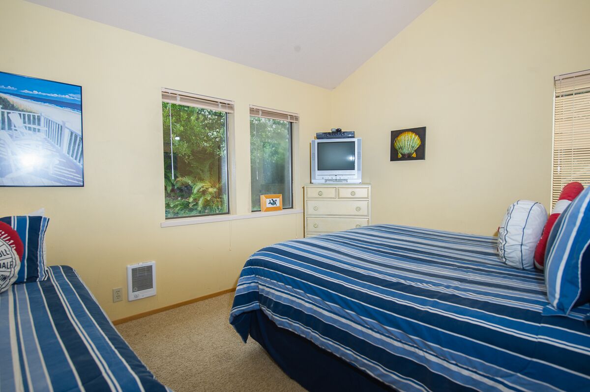 A bedroom with two beds, a television, a dresser, and a window with a view of trees.