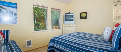 Un dormitorio con dos camas, televisión, cómoda y ventana con vista a árboles.