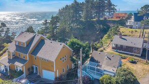 Une maison jaune avec un garage, entourée d’arbres et offrant une vue sur l’océan.