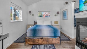Une chambre à coucher avec un lit, une cheminée, une télévision et une fenêtre donnant sur une maison.