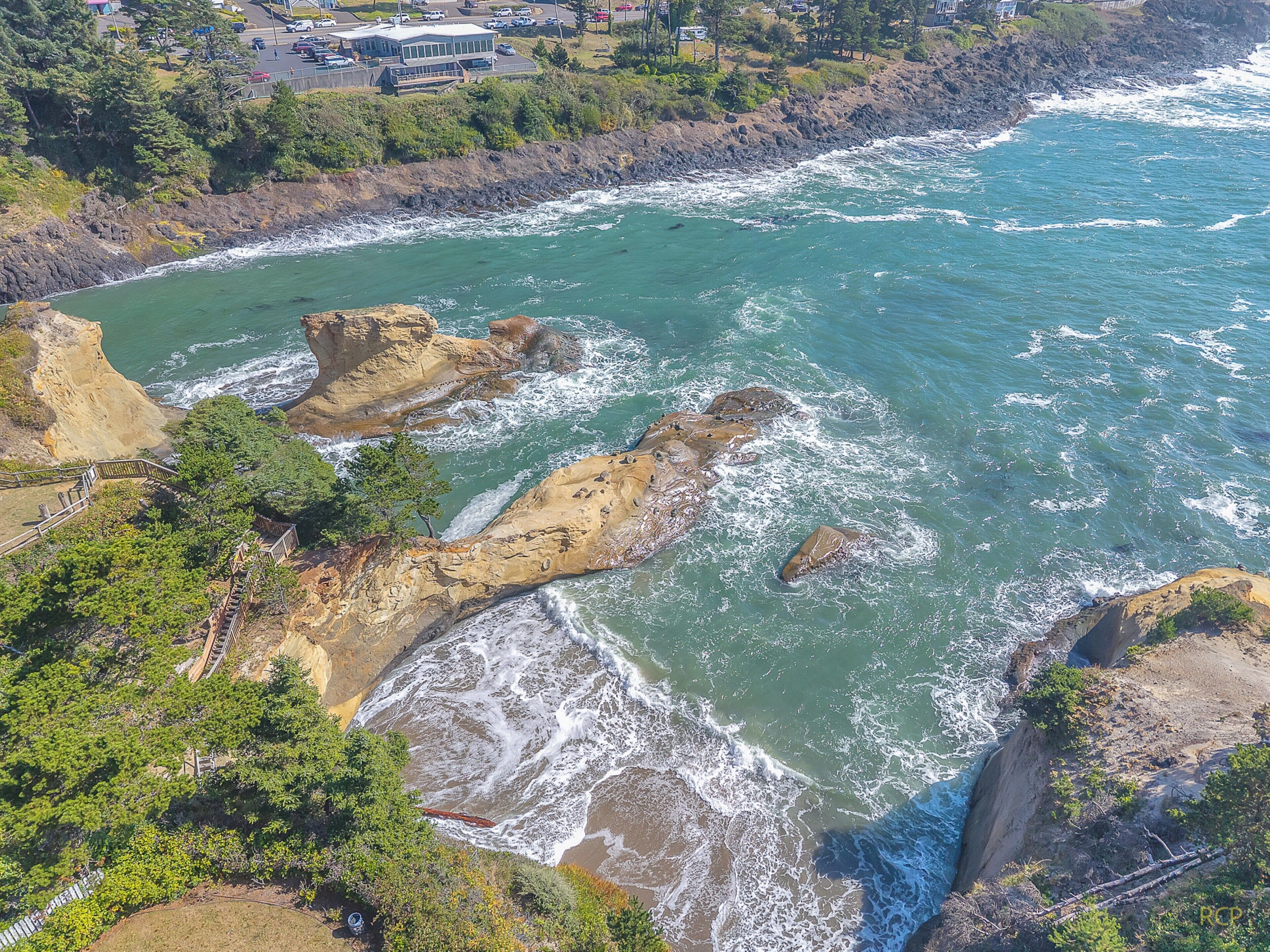 A coastal area with rocky cliffs, a beach, and a building with a large window overlooking the ocean.