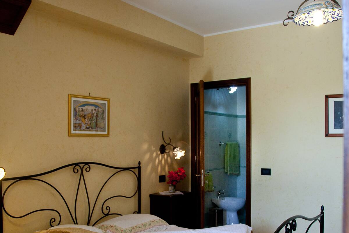A bedroom with a bed, a bedside table, a mirror, a window, and a door.