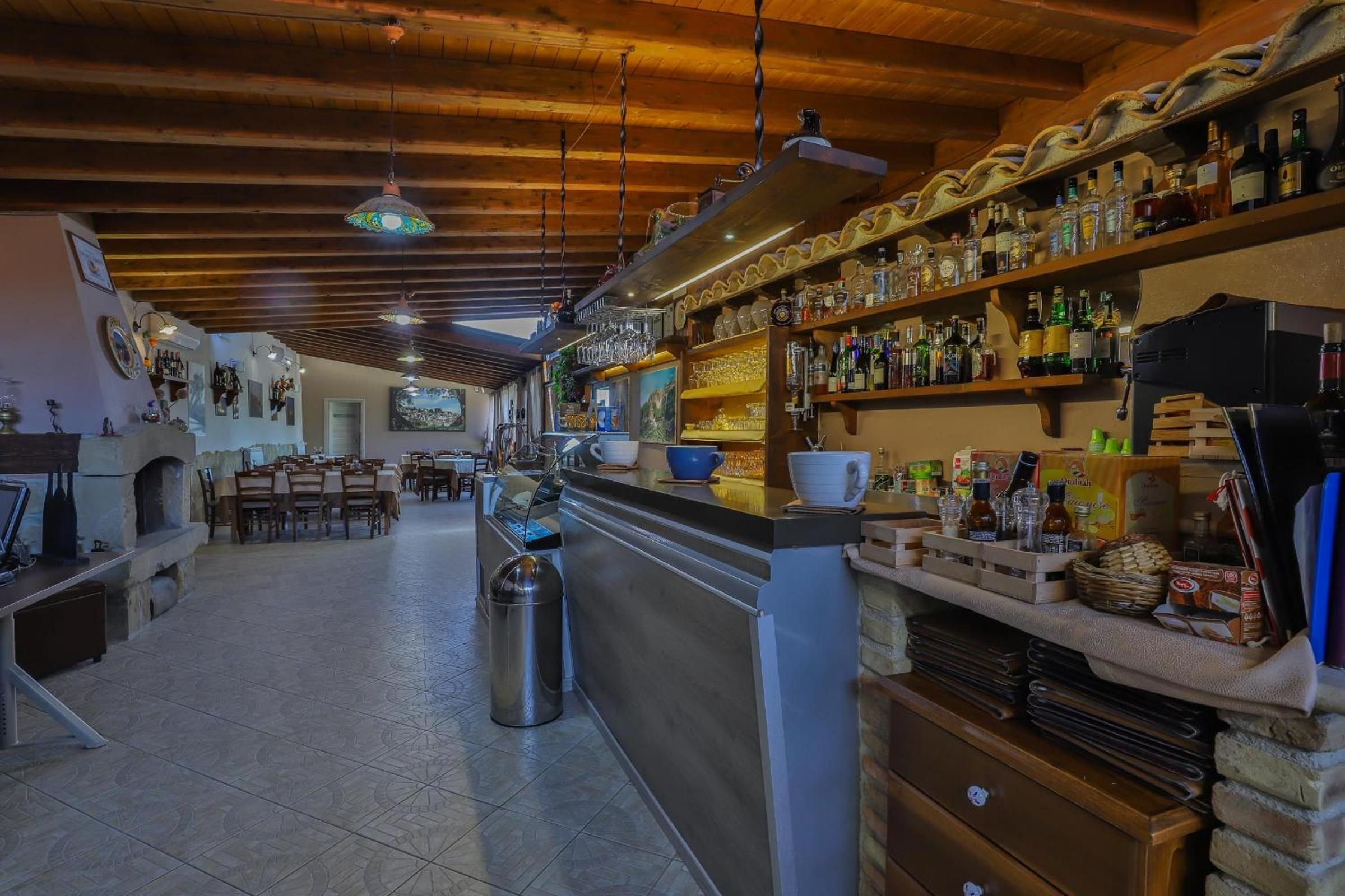 Un espace bar avec un long comptoir, des étagères remplies de bouteilles et un sol carrelé.