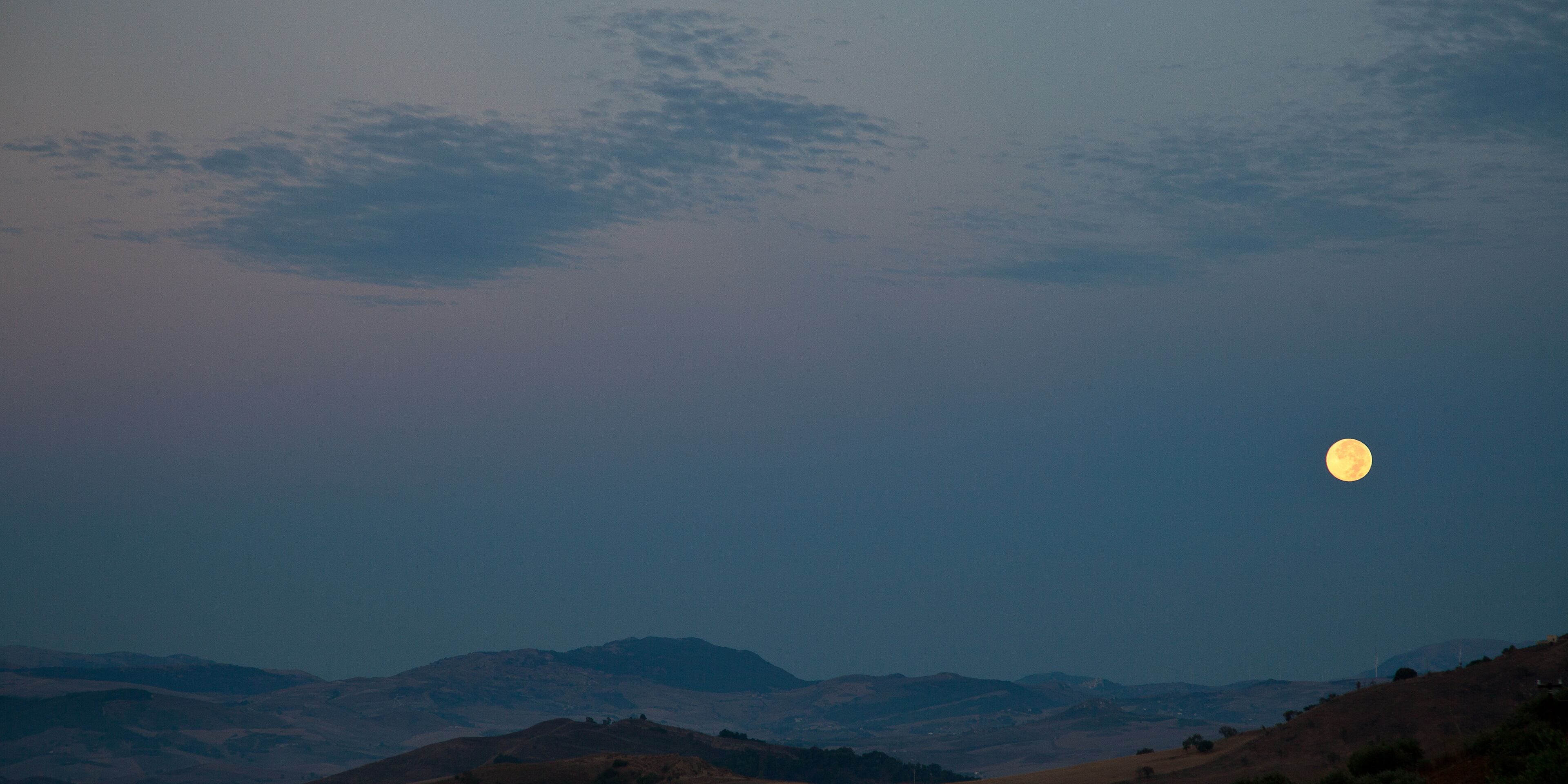 A landscape with a large moon in the sky, rolling hills, and a clear horizon.