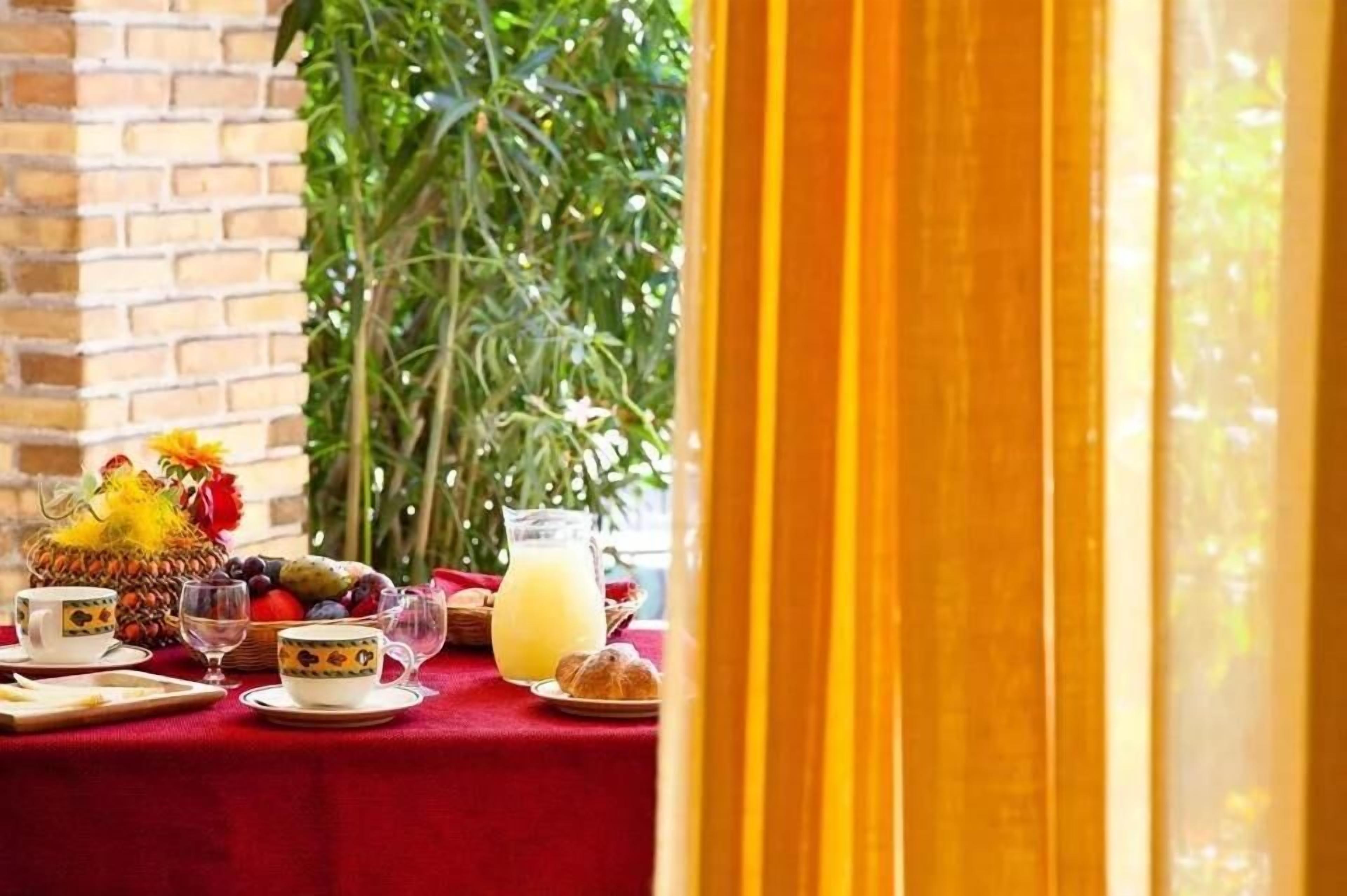 A breakfast table with a red tablecloth, fruit, pastries, and a pitcher of orange juice.
