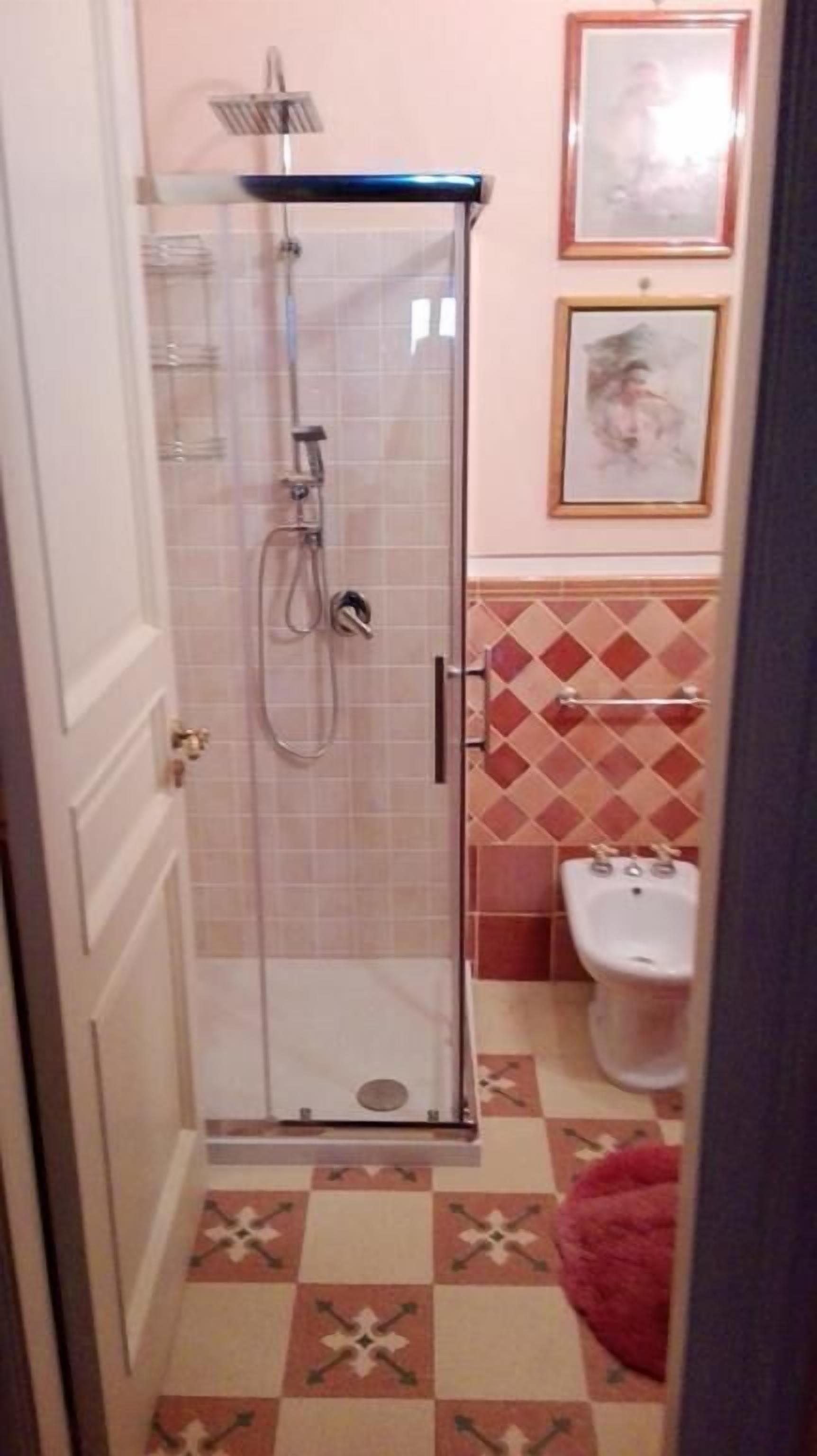 Un baño con ducha envuelta en vidrio, inodoro y azulejos de suelo estampados.