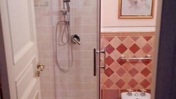Un baño con ducha envuelta en vidrio, inodoro y azulejos de suelo estampados.