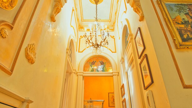 An ornate hallway with a chandelier, framed artwork, and architectural details. - B&B Flora House (Salerno)