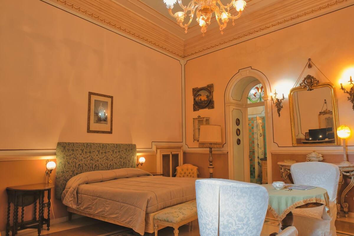 A hotel room with a bed, a chair, a table, and a mirror.