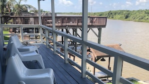 A covered deck with white plastic chairs and a wooden deck extending over a body of water.