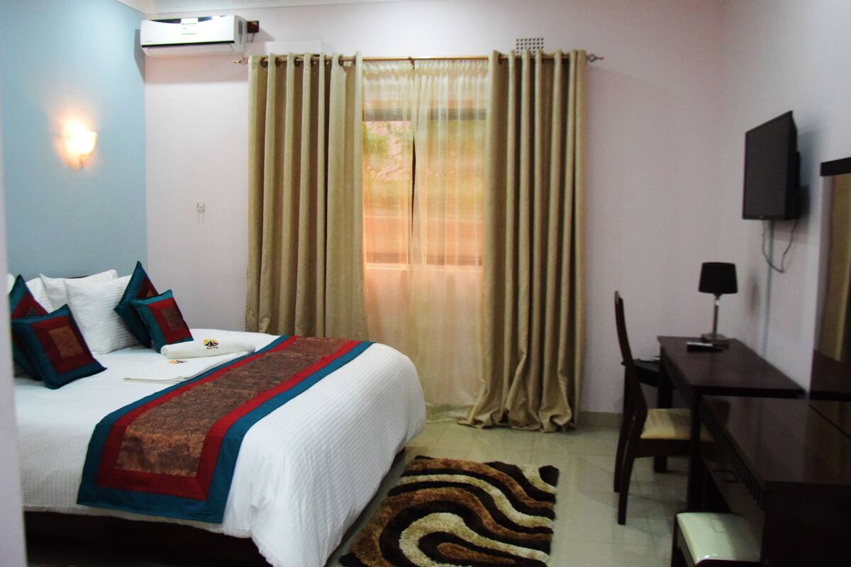 A hotel room with a bed, a desk, a chair, a television, and a window with curtains.