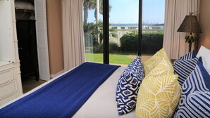 Een slaapkamer met een bed, uitzicht op zee en een balkon met gordijnen.