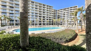 Een meerlaags hotel met een centraal gelegen zwembad, omgeven door palmbomen en een verzorgde tuin.