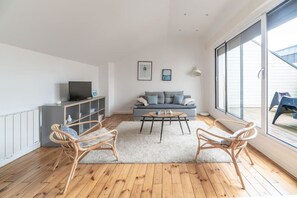 Ein modernes Wohnzimmer mit einem grauen Sofa, zwei Korbstühlen, einem Couchtisch und einem Fernseher auf einer Kommode.