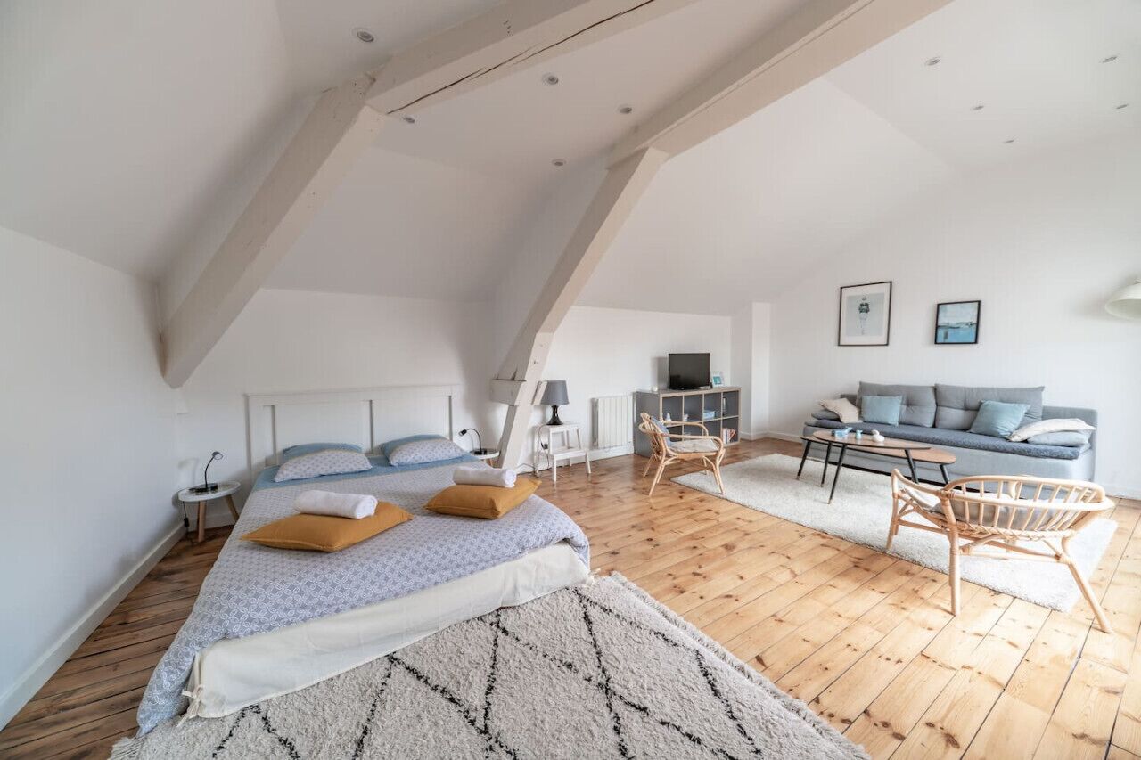 A spacious loft bedroom with a large bed, a sitting area with a sofa and chairs, and a television.