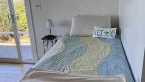 Een slaapkamer met een bed, een kussen met de tekst 'RELAX', een lamp en een uitzicht door een deur naar een buitenruimte.